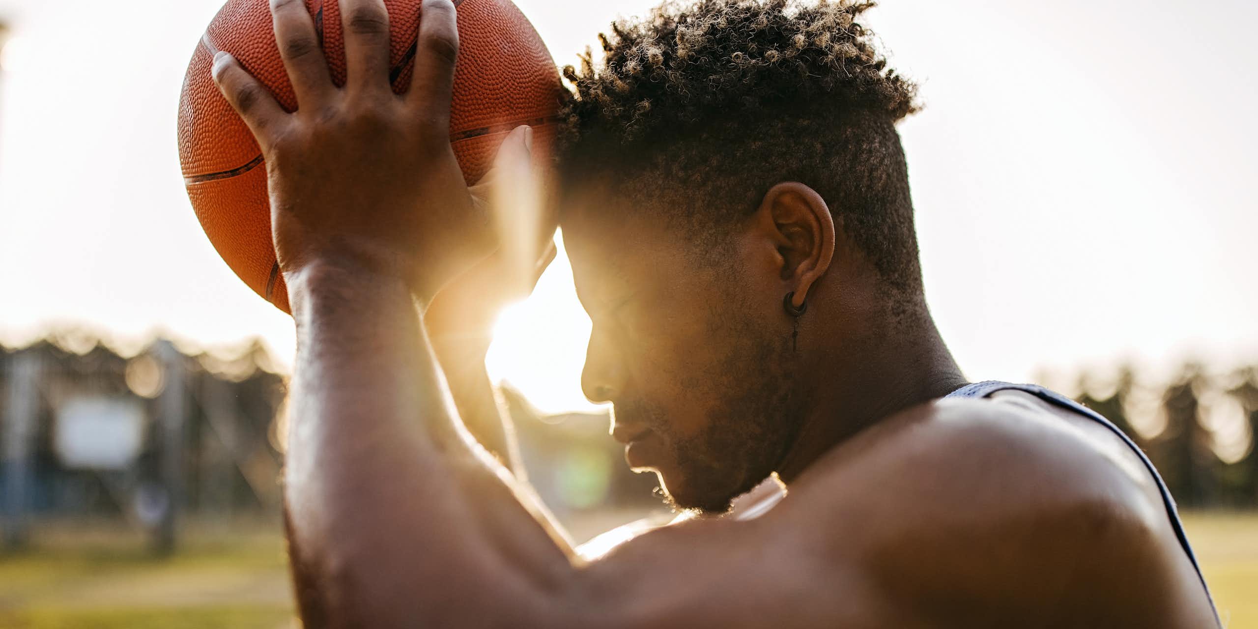 Young man wearing jersey holds basketball against forehead