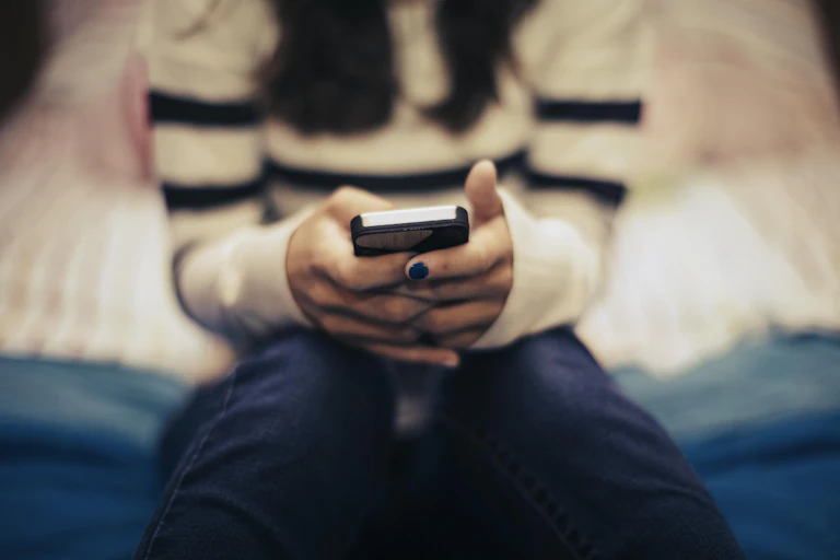 young person's hands with black fingernail polish hold a smartphone