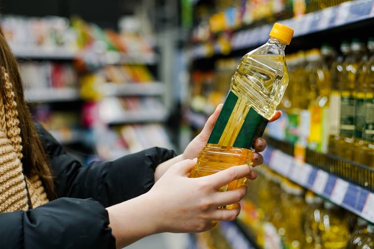 A person holds some sunflower oil while standing in a supermarket.