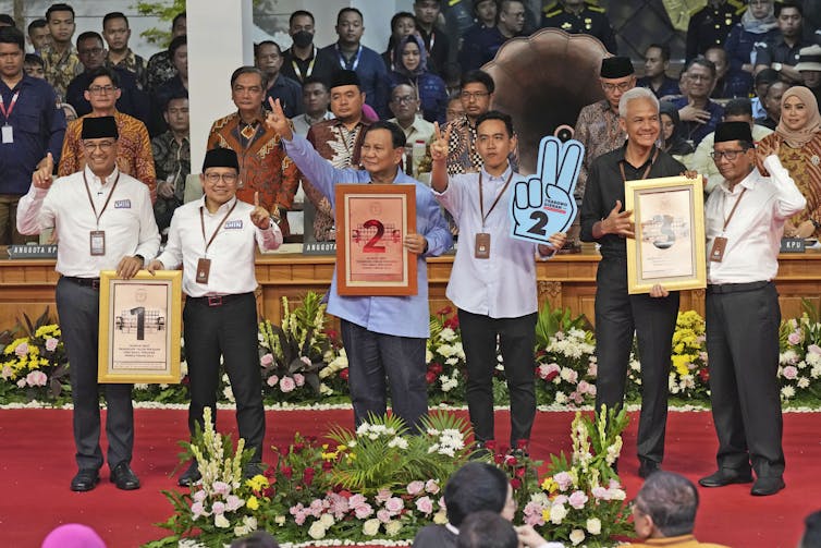 A group of men stand smiling and waving.