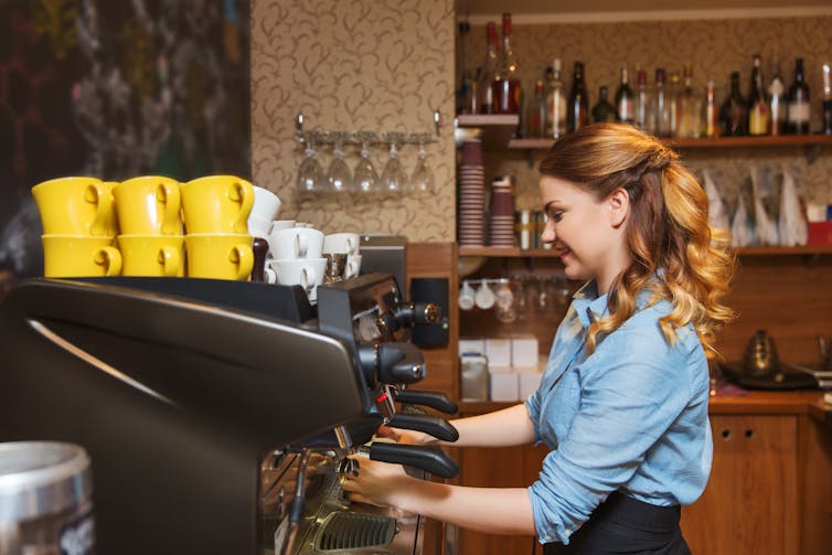 Young woman using a machine to make coffee in a cafe