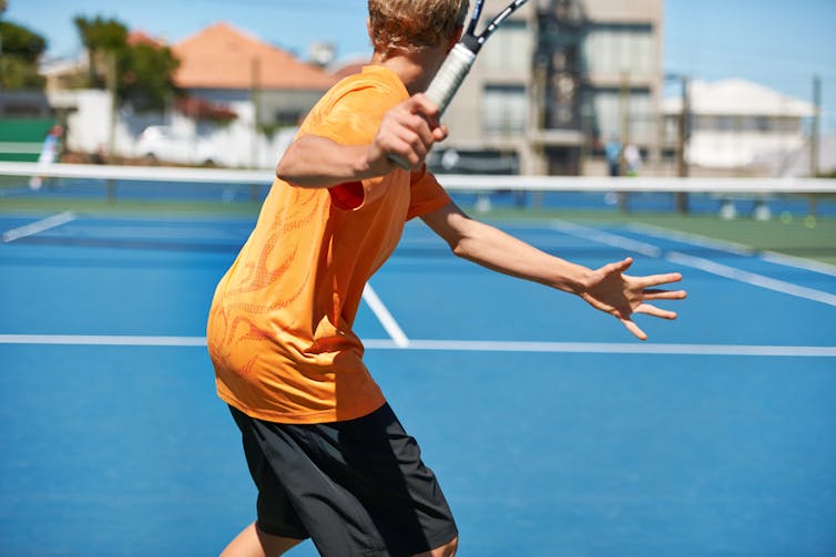 Young boy with back to the camera playing tennis