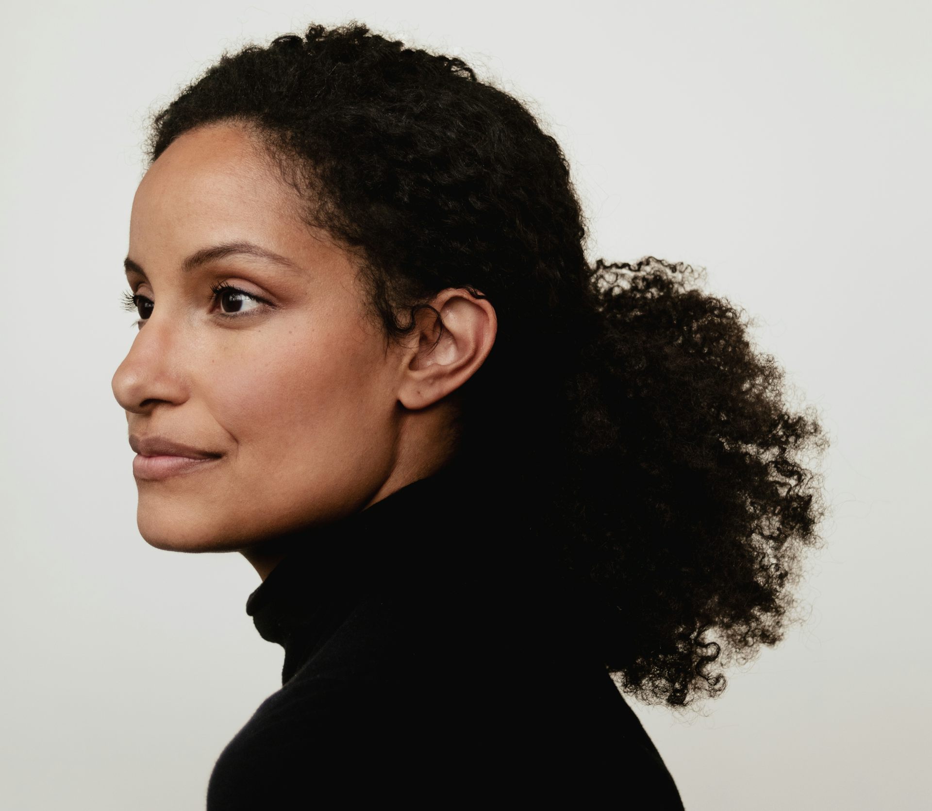 Smiling Black woman in profile with black turtleneck and ponytail