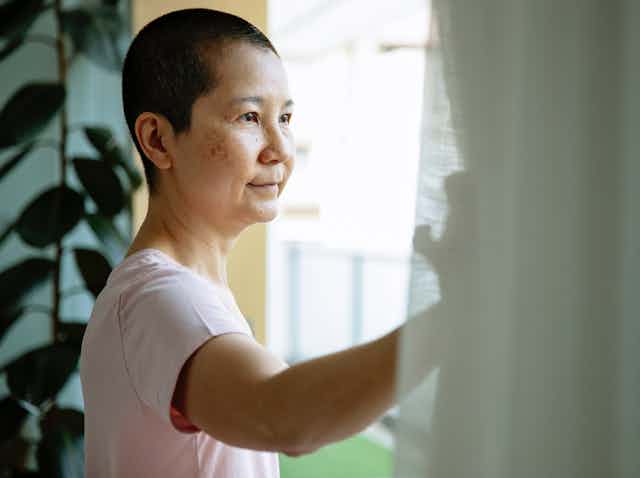 Woman undergoing cancer treatment looks out the widow