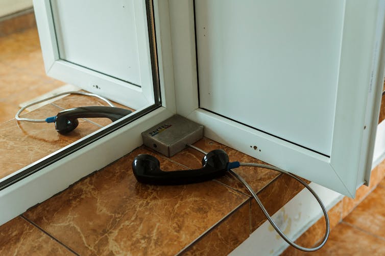 A phone on a metal cord on one side of a glass visitor booth in a prison