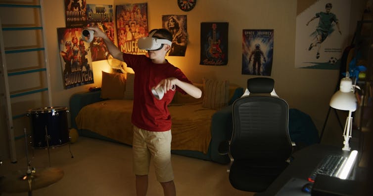 Young boy in VR headset stands in his bedroom and uses wireless controllers in his hands
