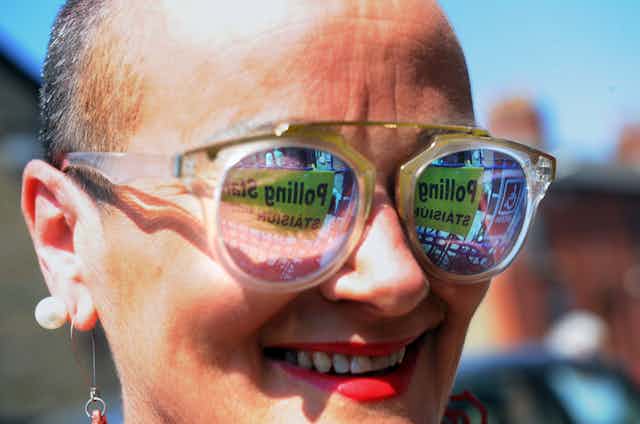  A woman outside a polling station with the "polling station" sign reflecting off her glasses.