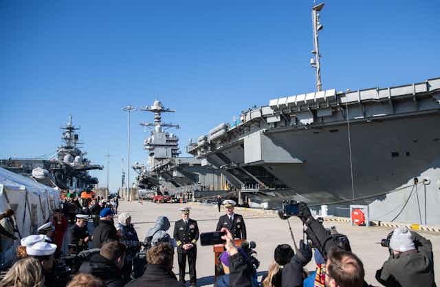 US naval officers pose for photos in front of the new aircraft carrier, the USS Gerald Ford.