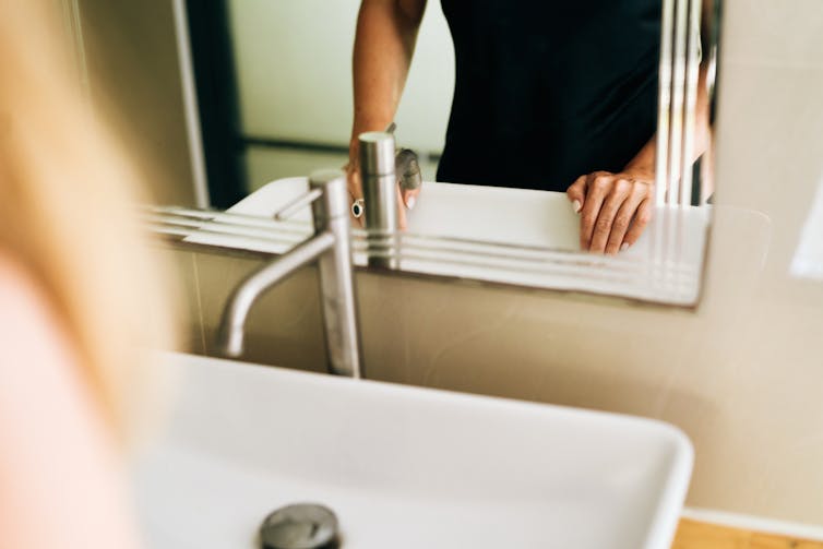 Behind-the-shoulder view of a bathroom mirror reflection of someone's hands gripping the sink