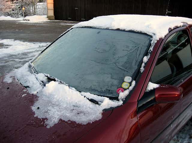 A snow-covered car with a thin layer of feathery ice covering the windshield. 