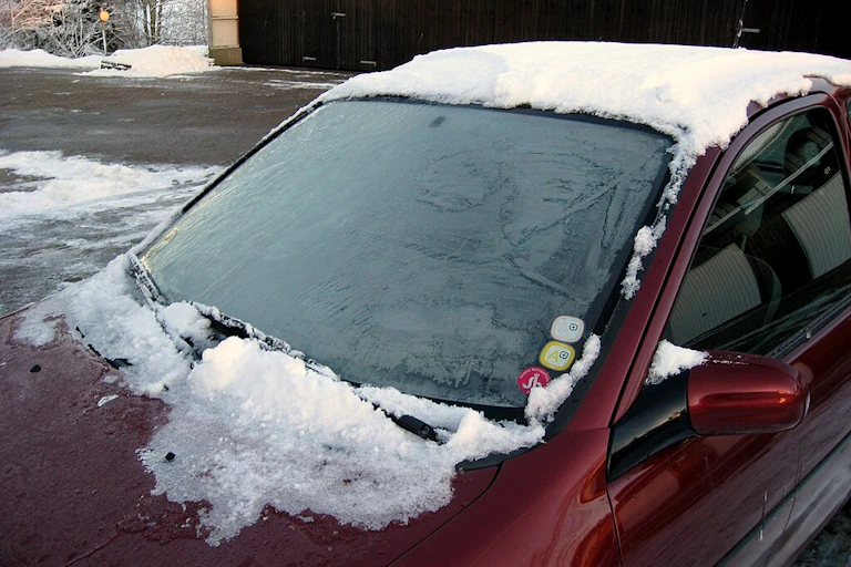 A snow-covered car with a thin layer of feathery ice covering the windshield.