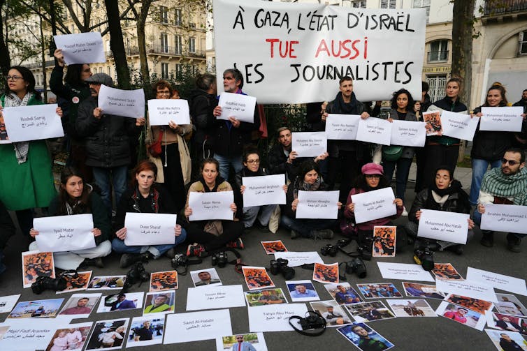 Protestors hold a banner which reads 'In Gaza, the State of Israel also kills journalists,' while displaying names and photographs of those killed on the ground.,