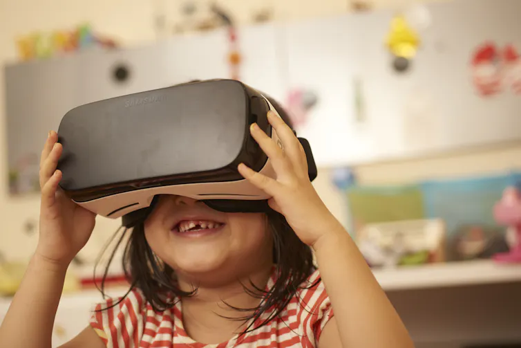 A very young girl holding a VR device on her face and smiling