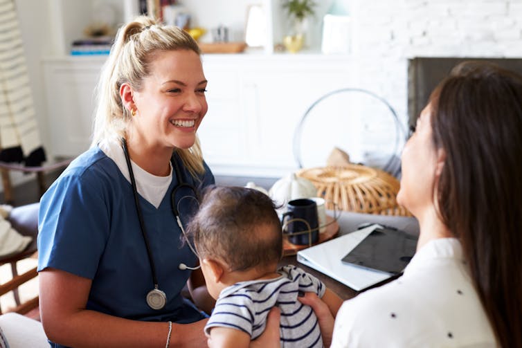 A smiling health-care worker consults with a mum and her baby.