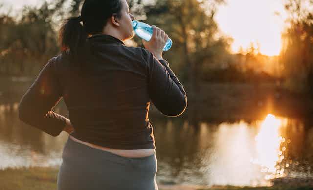 Woman drinks water looking at the sunrise