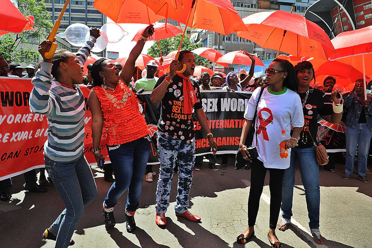 Women and men holding up open red umbrellas and banners while on a street