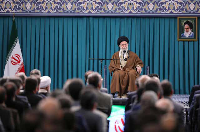 Iranian supreme leader, Ayatollah Ali Khamenei sits ona stage in front of an audience, delivering an economic briefing,