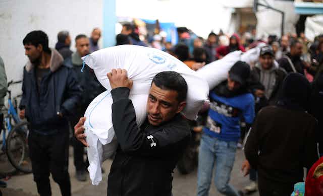Palestinians walk through the southern Gaza Strip city of Rafah carrying sacks of food provided by UNRWA