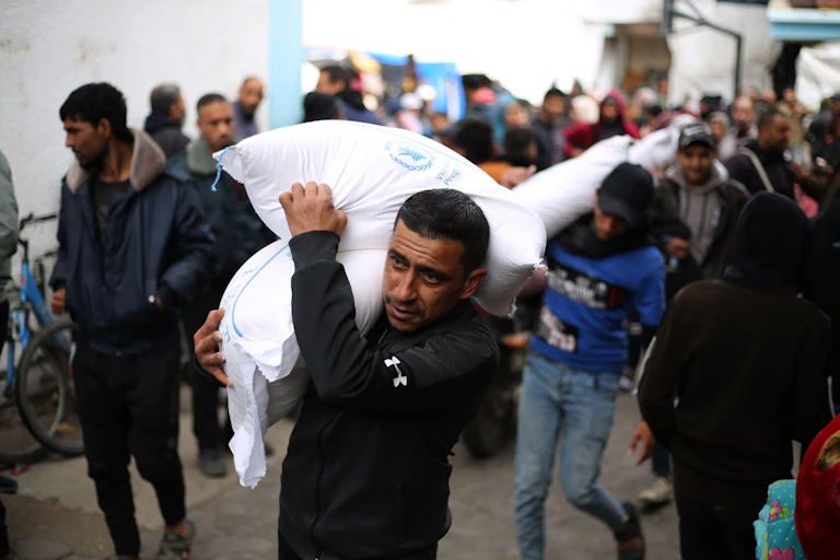 Palestinians walk through the southern Gaza Strip city of Rafah carrying sacks of food provided by UNRWA
