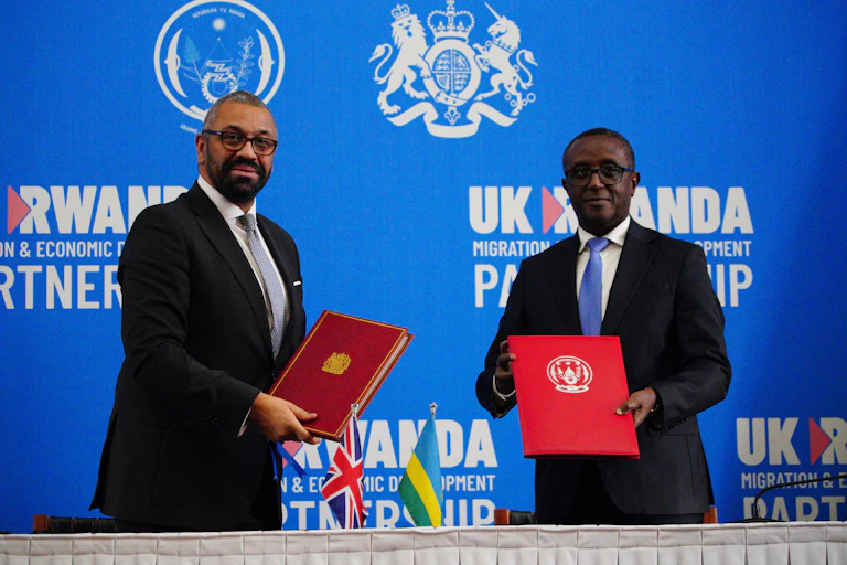 James Cleverly and Vincent Biruta holding red folders in front of a blue backdrop reading UK Rwanda partnership