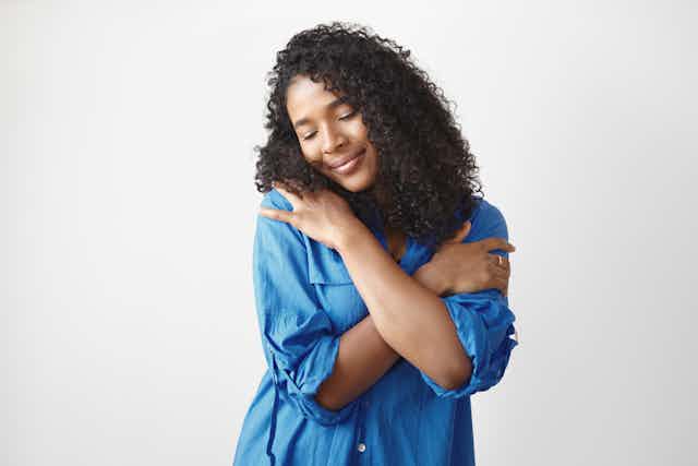 Young woman in blue shirt giving herself a hug