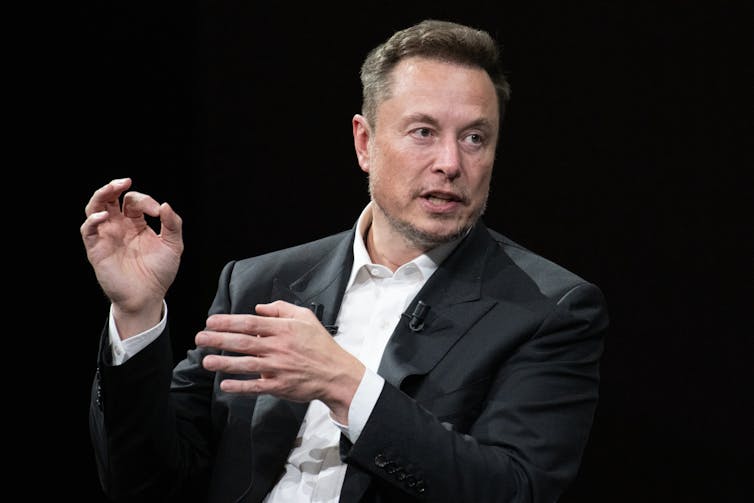 A middle-aged man in a suit gestures while speaking