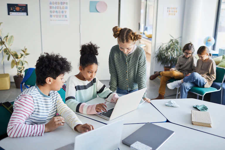 Elementary or middle school students work on laptops at a table.