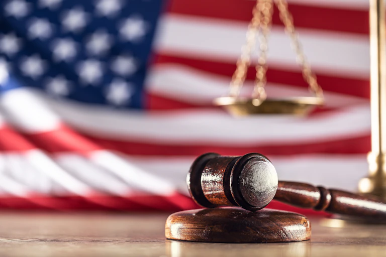 A gavel and a scale sit in front of a U.S. flag.