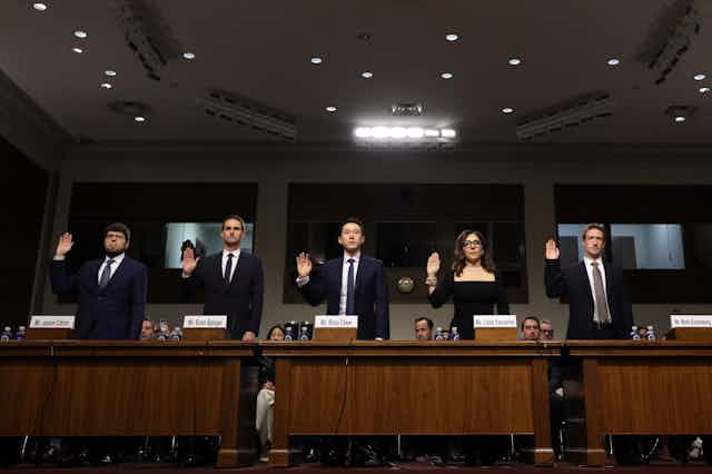 five people in business attire stand with their right hands raised