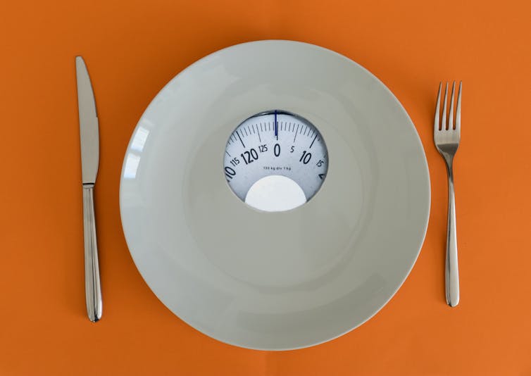 White plate with scales, knife and fork on an orange background.
