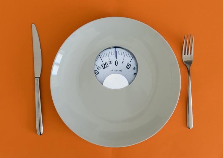 A white plate with a weighing scale, knife and fork, against an orange background