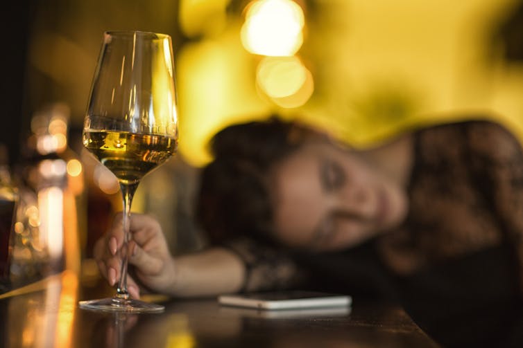 a woman passed out on a table, holding a glass of white wine