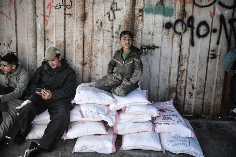 A boy sits on top of bags of flour.