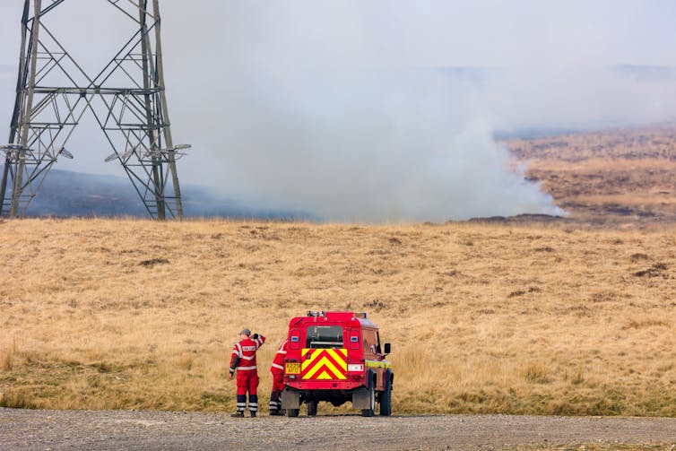 A moorland with smoke rising from it and a fire engine in the foreground.