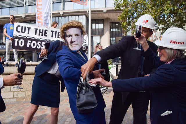 Protesters dressed as oil executives stuff the purse of 'Keir Starmer' with cash.