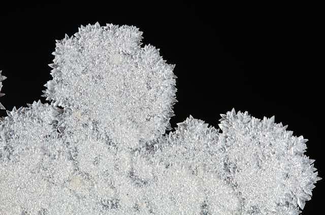 White, flaky crystal growths photographed against a black background.