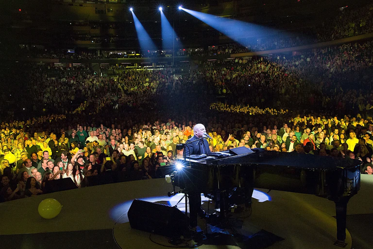 Bald man plays piano on stage in front of thousands of fans.