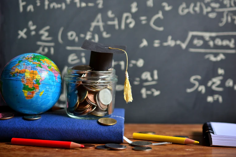 Pièces de monnaie et globe devant un tableau noir et des crayons de couleur