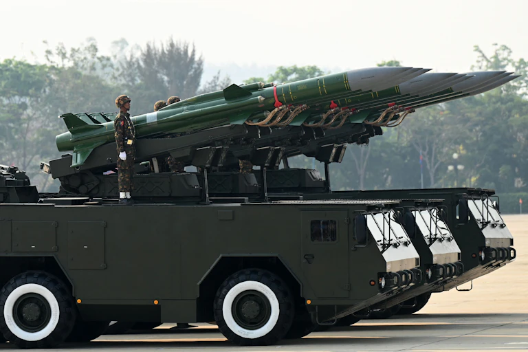 A man in military uniform stands on a rocket launcher.