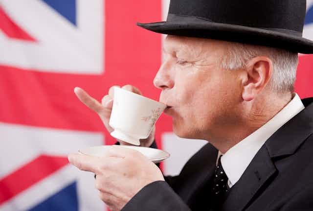 View of a well-dressed man sipping a cup of tea in front of a union jack flag