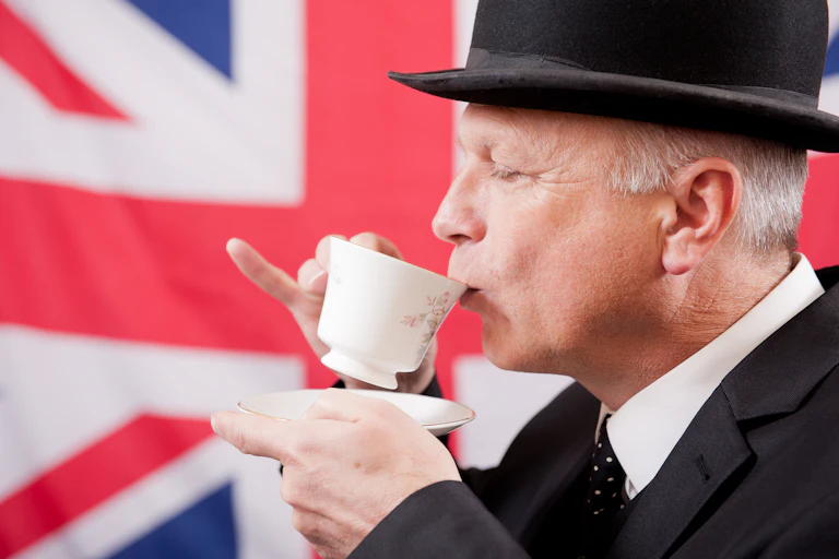 View of a well-dressed man sipping a cup of tea in front of a union jack flag