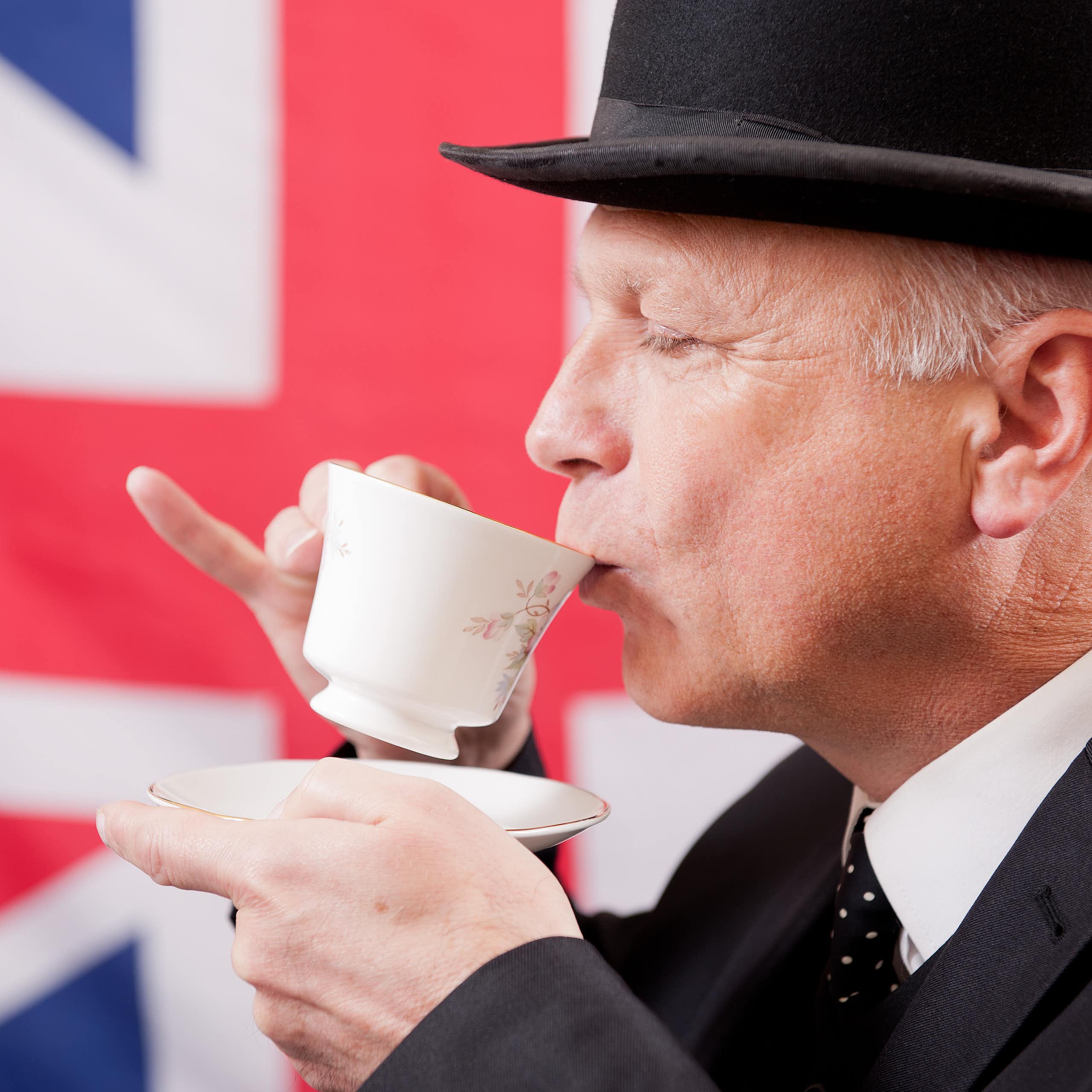 View of a well-dressed man sipping a cup of tea in front of a union jack flag