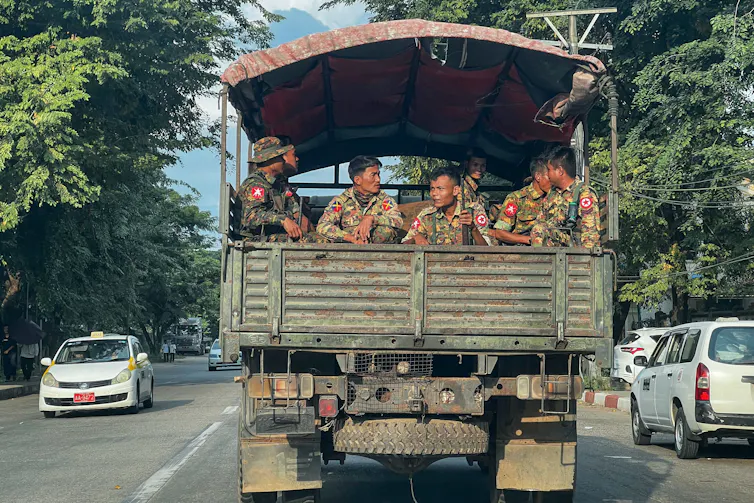Men in fatigues ride on a military vehicle.