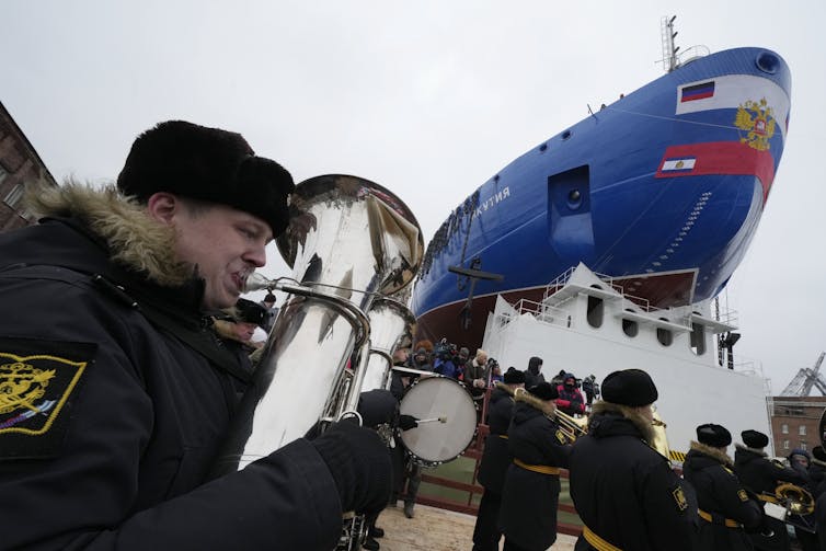 A band plays near a large ship.