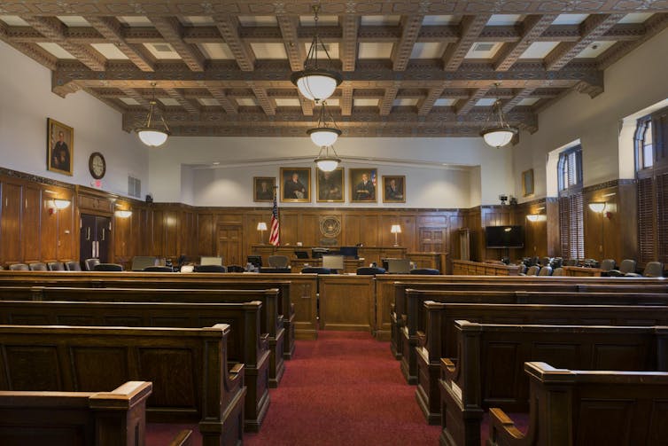 A view of a courtroom from the rear, showing seating and, down the aisle, the bench where a judge sits.