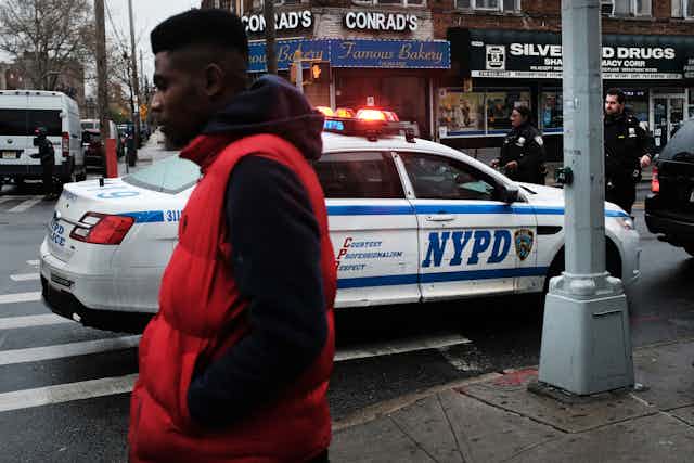 Man walks past NYPD patrol car in Brooklyn 