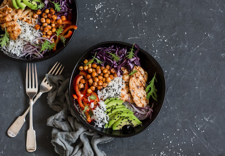 A bowl containing bright, fresh vegetables, chicken and chickpeas sits on a table.