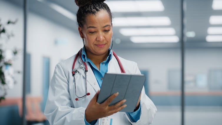 A woman in a white coat and stethoscope with an iPad