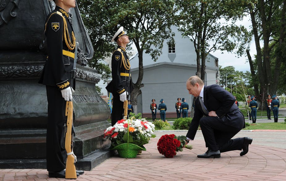 Putin on his knees with a bunch of flowers at a monument to Peter the Great.
