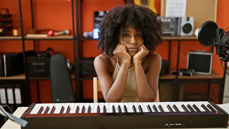 mulher negra sentada em um teclado, com cara de cansada.